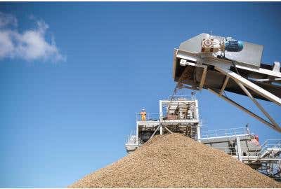 Mining worker standing on elevated platform watching dirt be poured out of construction machinery.