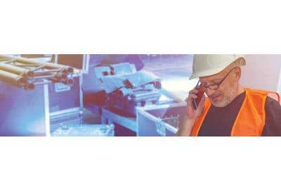 Construction worker holding plans and talking on cell phone, with pipes in the background