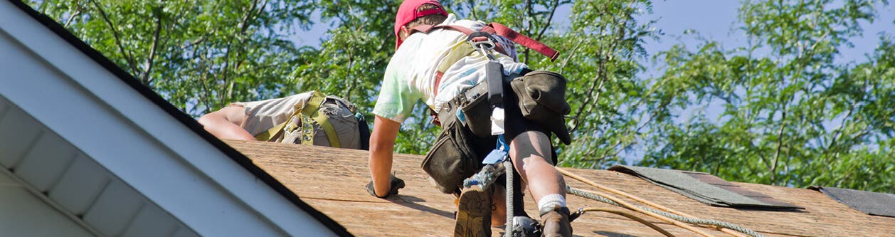 Worker on a roof with Fall Protection harness and other safety gear