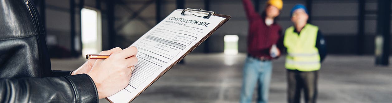 Inspector holding clipboard with form while two workers stand in the background