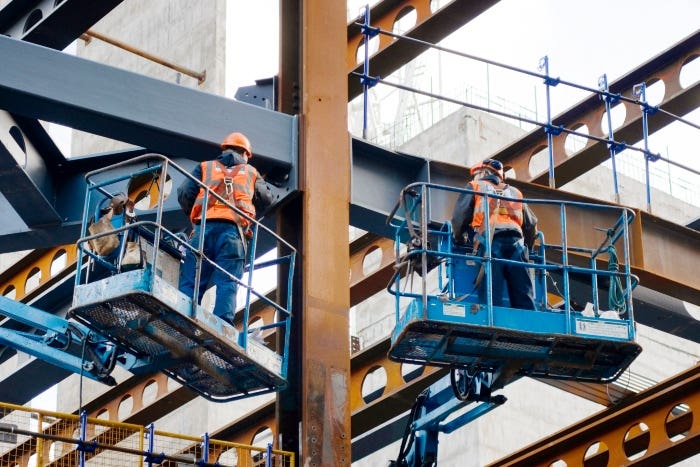 Two workers standing on elevated platforms wearing fall protection gear